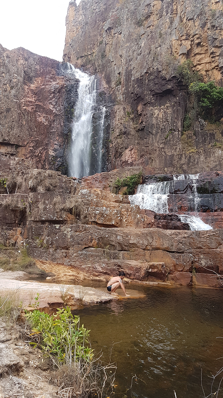 Homem abaixado molha mão na cachoeira Catedral vista da piscina do andar inferior