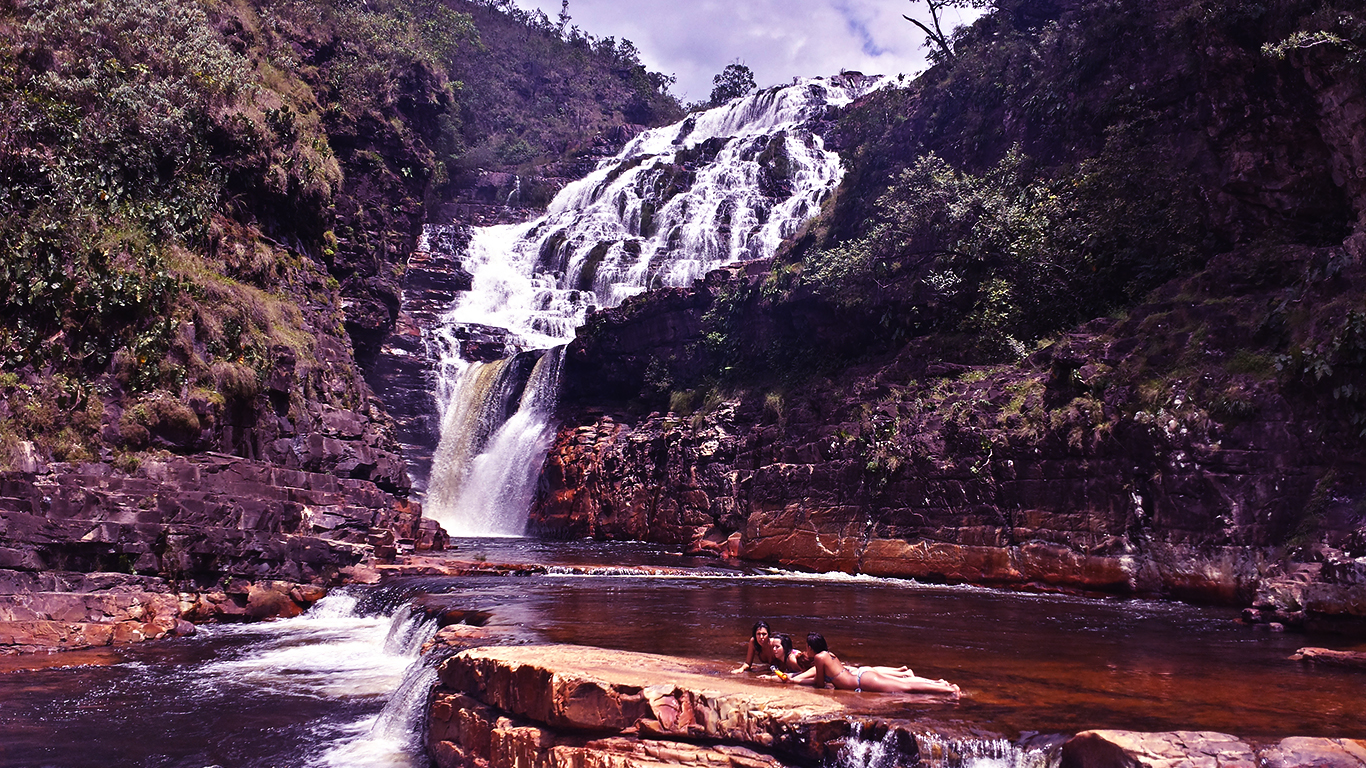 Turistas pegam sol na última piscina natural das cataratas dos Couros no período de seca com as cachoeiras almécegas 1000 e do Parafuso no fundo na Chapada dos Veadeiros