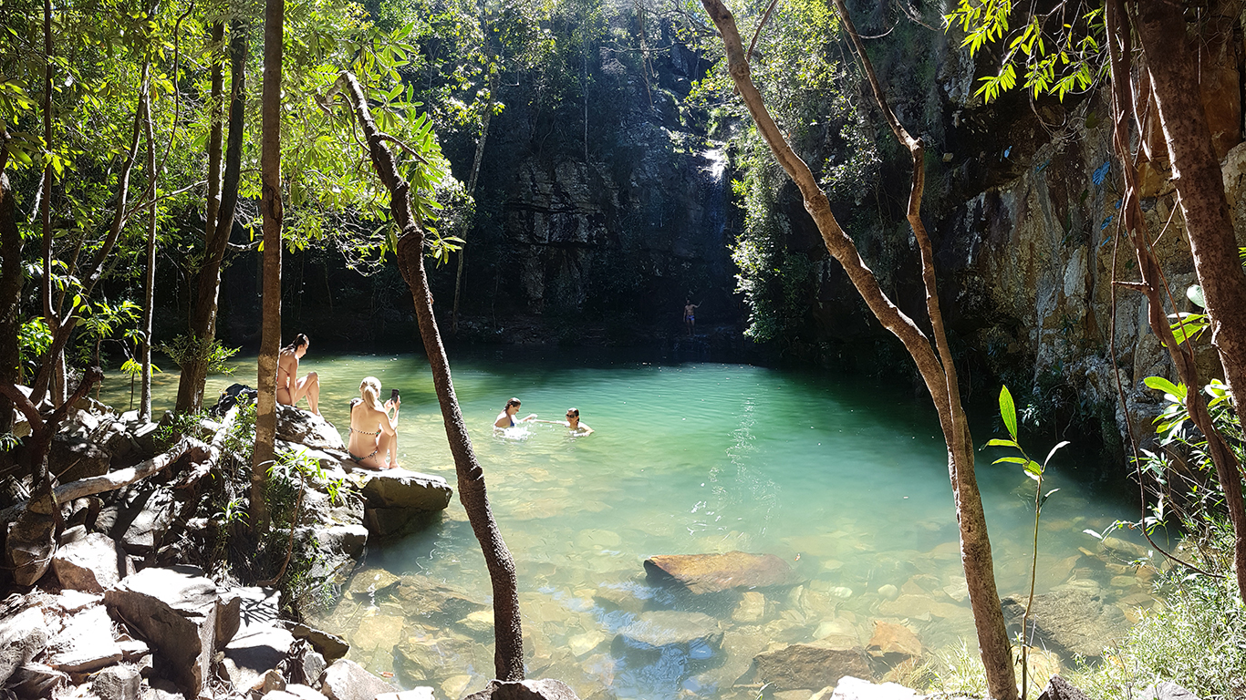 Visitors at Poço do Sol, Loquinhas waterfall, Chapada dos Veadeiros, rainy season — green water between rocks and forest